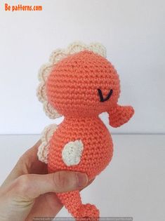 a hand is holding an orange crocheted stuffed animal with white ears and tail