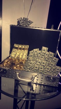 a suitcase filled with money sitting on top of a glass table next to a pile of gold coins