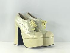 1970s light gold colored leather glam rock platforms by Emma of London. Are a lace-up shoe with brough detailing which is the pattern of holes and marks on the upper of the shoe. Have high platforms and heels. Look like a 90s platform but because of the construction, soles, and label, I think they are 70s. Condition: very good vintage condition. Completely wearable. The leather color has been touched up through the bottom part of the shoes because they were heavily scuffed. Label: Emma of London. Circa: 1970s Composition: leather upper and socklining, manmade sole Color: light gold, slightly metallic Size: unlabeled  Fits like: 7 (us) / 37.5 (eu) / 4.5  Measurements: Length of insole: 9.8" (25.9 cm) Width of insole: 2.8" (7.3 cm) Toe platform: 2.2" (5.7 cm) Heel: 5.5" (14 cm) Gold Platform Shoes, Tall Heels, Platform Oxfords, Gold Platforms, Light Gold Color, Oxford Platform, Glam Rock, Colored Leather, Gold Leather