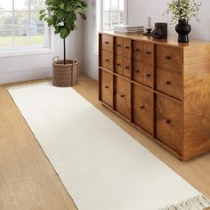 a white rug on top of a wooden dresser next to a potted plant and window