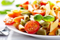 a white plate filled with pasta and vegetables on top of a table next to a fork