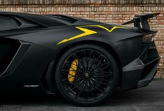 the black and yellow sports car is parked in front of a brick wall with an arrow painted on it