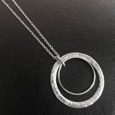 This women's hammered silver two circle pendant necklace is crafted with stainless steel making it waterproof, tarnish resistant. Polished to a mirror finish, this 1.25 inch diameter pendant strikes an elegant balance between subtlety and breathtaking style, making it perfect for any occasion. Available in your choice of chain length from 16 to 24 inch. With its timeless appeal, this handmade necklace is sure to be a treasured piece in your jewelry collection for years to come. Modern Hammered Round Necklace, Hammered Metal Round Necklaces, Hammered Metal Round Necklace, Modern Hammered Necklace With Round Pendant, Nickel Free Metal Necklaces, Nickel-free Circular Metal Necklace, Modern Hammered Round Pendant Necklace, Hammered Metal Circle Jewelry, Modern Hammered Metal Necklace