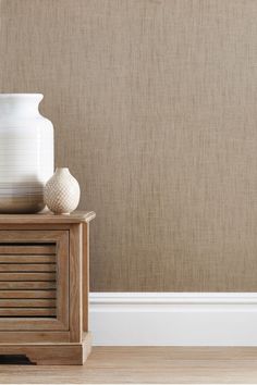 a white vase sitting on top of a wooden table next to a wall mounted clock