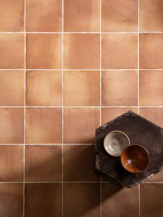 two bowls are sitting on a table in front of a brown tile wall with hexagonal tiles