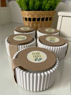 four cupcake tins sitting on top of a counter next to a basket filled with green plants