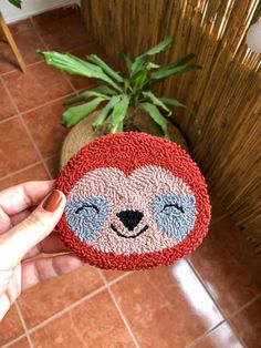 a hand holding a red and blue stuffed animal on top of a tile floor next to a potted plant