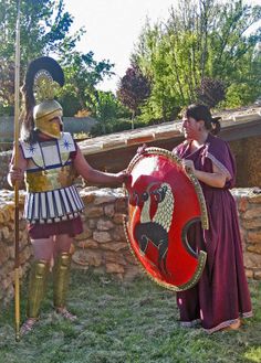 two people dressed in roman costumes standing next to each other and one holding a shield