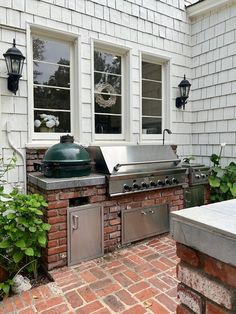 an outdoor kitchen with grills and potted plants on the side of it, in front of a white brick house