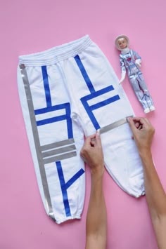 two hands are working on a pair of white sweatpants with blue and silver stripes