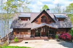 a large wooden house sitting on top of a lush green hillside next to a lake