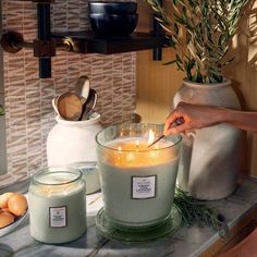 a person lighting a candle in a glass bowl on a counter top next to eggs