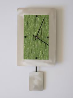 a square white clock with green grass on the front and sides, against a white wall