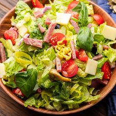 a salad with lettuce, tomatoes, cheese and ham in a wooden bowl