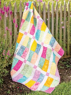 a patchwork quilt hanging on a fence in front of some pink and yellow flowers