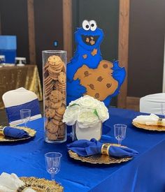 a blue table topped with plates and vases filled with cookies next to a cookie monster