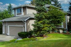 a house with trees in the front yard and grass on the side walk to the driveway