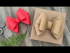 two paper bows sitting on top of a piece of cardboard next to scissors and greenery