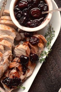 sliced meat with cherries and cranberry sauce on a white serving platter