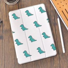 an ipad case with green dinos on it next to some pens and pencils