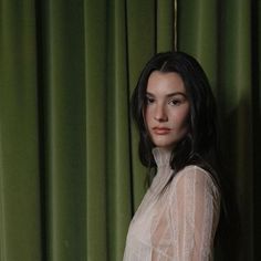 a woman standing in front of green curtains with her hands on her hips and looking at the camera