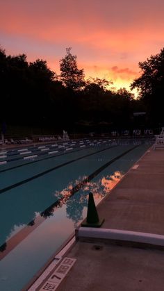 an empty swimming pool at sunset with the sun setting in the distance and trees behind it