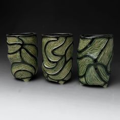 three green vases sitting next to each other on a gray surface with swirl designs