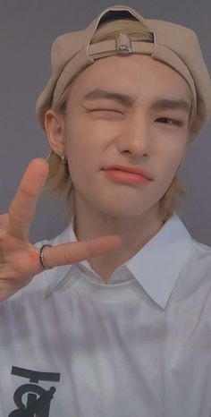 a young man making the peace sign with his hand and wearing a hat on top of his head