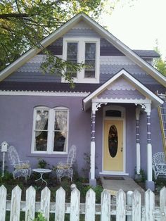 a purple house with white picket fence around it and two chairs in the front yard