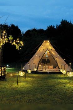 a tent is lit up at night with fairy lights on the grass and trees in the background