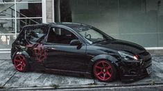 a small black car with red rims parked in front of a building