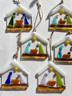 six glass ornaments hanging from twine on a white wall, each decorated with different colors and shapes