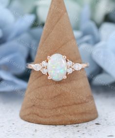 a white opal and diamond ring sitting on top of a wooden stand