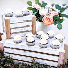 cupcakes are arranged on top of a wooden crate with flowers in the background