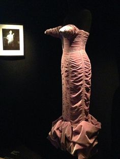 an old fashion dress is on display in a dark room next to a framed photograph