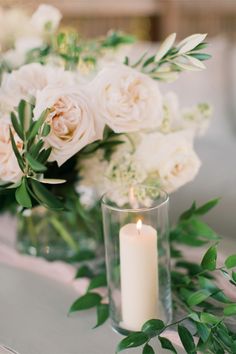 white flowers and greenery are arranged in glass vases with candles on the table