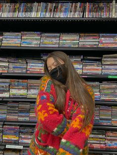 a woman wearing a face mask standing in front of a rack of dvd's