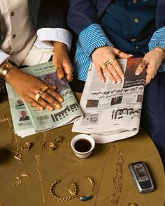 two people sitting next to each other with their hands on top of a newspaper and coffee