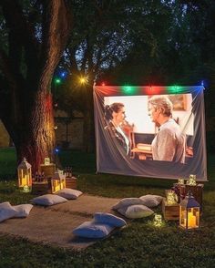 an outdoor movie screen with lights and pillows on the ground