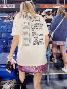 a woman in a white shirt and pink sequin skirt walks through the stands at a baseball game