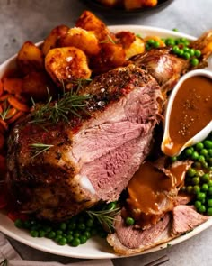 a plate full of roast, potatoes and peas with gravy on the side