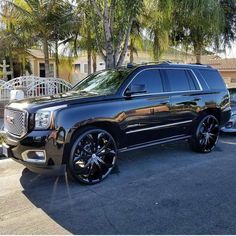 a black suv is parked in front of some palm trees and other cars on the street