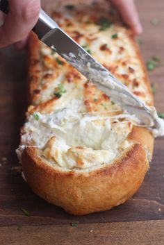 someone is cutting into a cheesy bread dish with a large knife on top