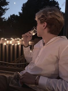 a man sitting on a porch drinking from a wine glass with string lights in the background