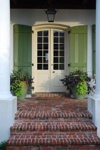 a white door with green shutters and potted plants on the steps to it