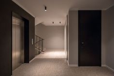 an empty hallway with black doors and white carpeted flooring is lit by recess lights