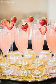 several glasses filled with pink liquid and topped with strawberries on a gold platter