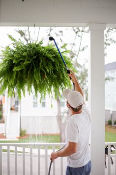 a man is watering the porch with a sprayer on it's head and holding a plant in his hand