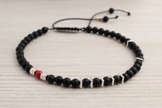 An asymmetric men's bracelet with black onyx stones, sterling silver spacers, and one red coral bead. The bracelet has one red coral bead as a focal point, adding a vibrant pop of color. It's a unique and bold accessory that combines contrasting elements, making a statement and adding individuality and style to any outfit. Details: 4mm matte black onyx 4mm red coral sterling silver spacers nylon cord Modern Beaded Bracelet With Black Beads As Gift, Modern Handmade Black Bracelets, Modern Black Beads Bracelets As Gift, Modern Black Beads Bracelet As Gift, Modern Black Beaded Bracelets As Gift, Modern Onyx Bracelets For Gifts, Modern Onyx Bracelets For Gift, Modern Black Beaded Bracelet For Gift, Modern Onyx Bracelets As Gift