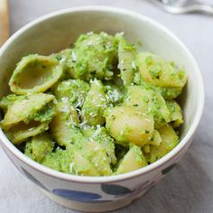 a small bowl filled with green food next to a fork and spoon on top of a table